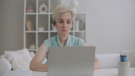 Eine-ältere-Frau-Mit-Headset-Spricht-Per-Webkamera-Und-Nutzt-Einen-Videoanruf-Zur-Kommunikation-Auf-Dem-Laptop